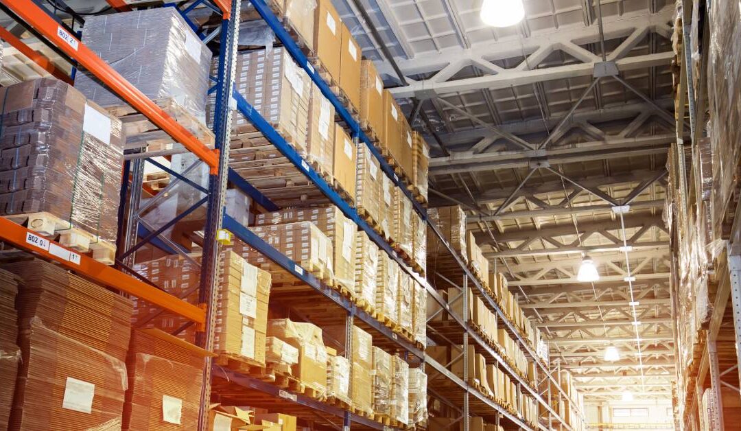 The interior of a large warehouse shows multiple shelves lined with neatly stacked products stretch into the distance.