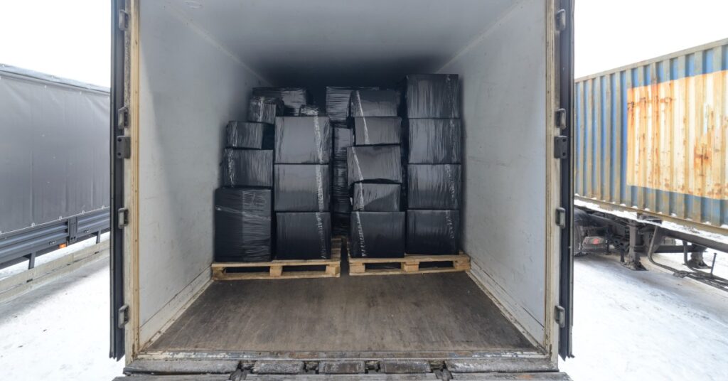 The back of a storage trailer with its door open. Inside of the trailer are large boxes wrapped in black plastic.