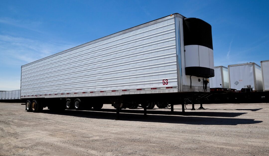 A large, white storage trailer is positioned in a gravel driveway. Several other storage trailers are lined up behind it.