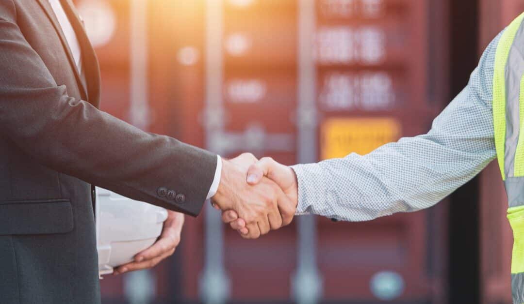 A close-up of two men's hands as they meet in the middle with a handshake in front of a red storage container.