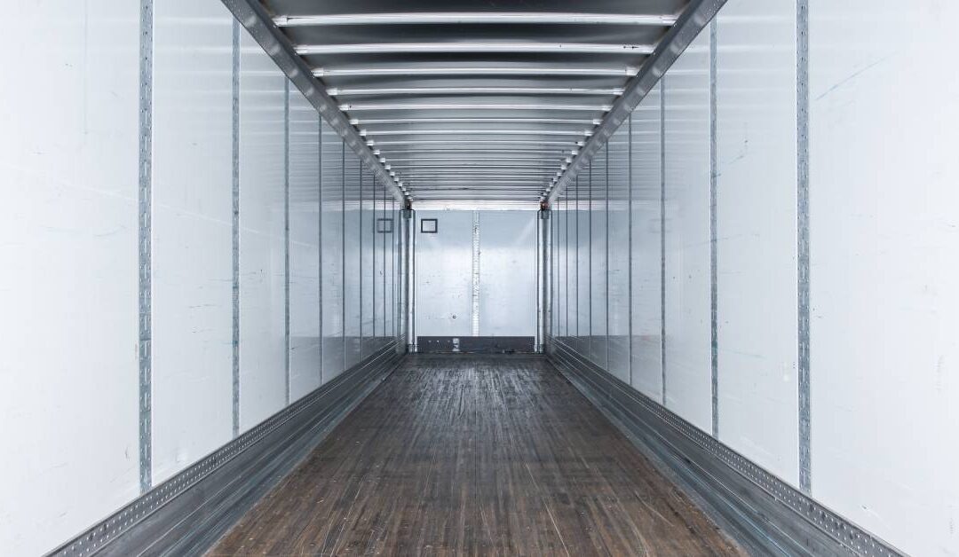 The interior of a dry van trailer is very neat and clean. It has white walls and a partially wooden floor.