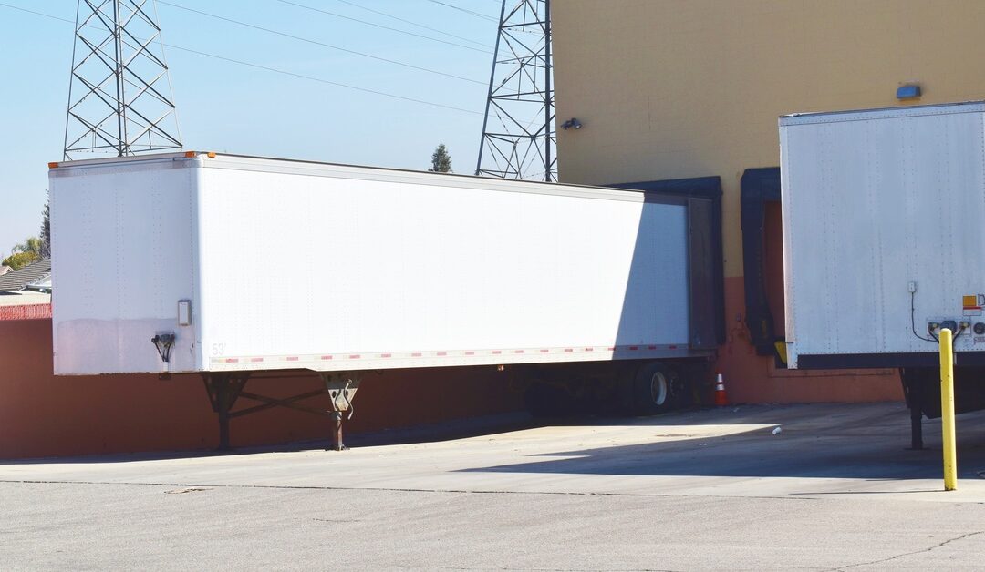 Two white trailers sit by a loading dock next to a yellow commercial building. In the distance are electrical transmission towers.
