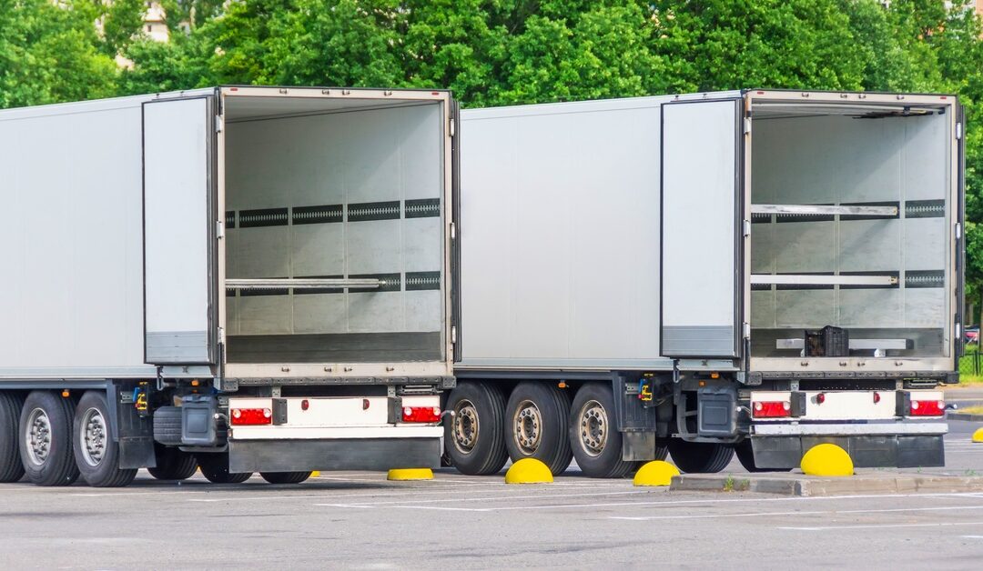 Two commercial trucks parked in a lot with open rear trailer doors, ready for loading cargo and goods.