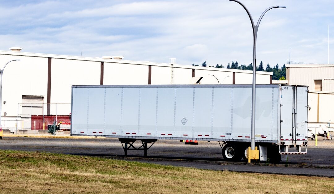 Semi tractor-trailer parked in a lot, shown from the side with the cab and trailer visible under daylight.