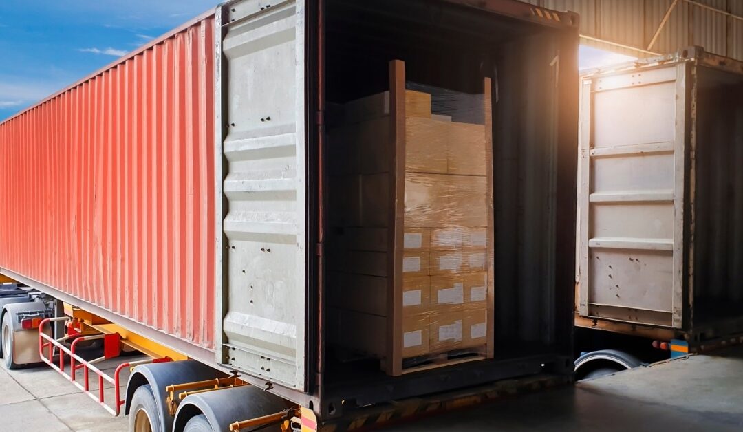 a red shipping container trailer with open doors and a pallet of wrapped boxes inside at a warehouse dock.
