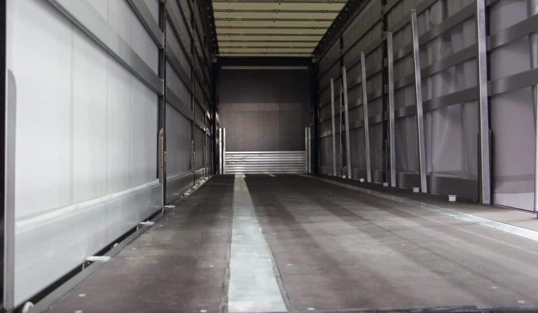 An empty truck trailer interior with gray side panels, a dark floor, and a pale center strip running lengthwise.