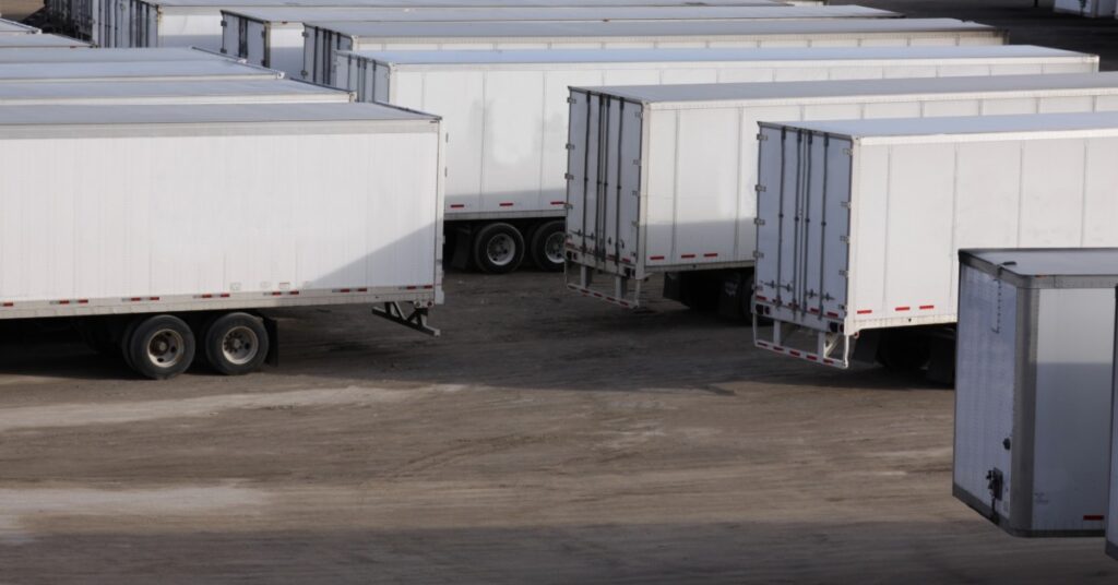 A group of white trailers parked closely together on a paved lot, with trailer doors and wheels visible.